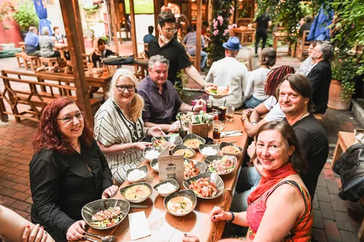 Eine große Runde am Tisch mit vielen Schalen, die Gäste schauen in die Kamera